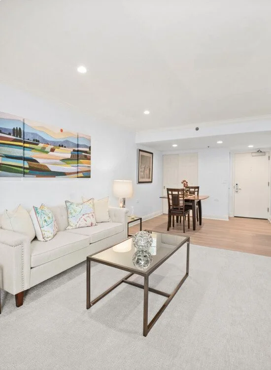 fully furnished, spacious living room and dining area with white rug and walls in senior living apartment