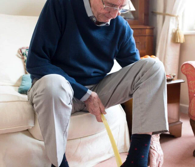 well-dressed senior man using shoe horn to put on his dress shoes while seated